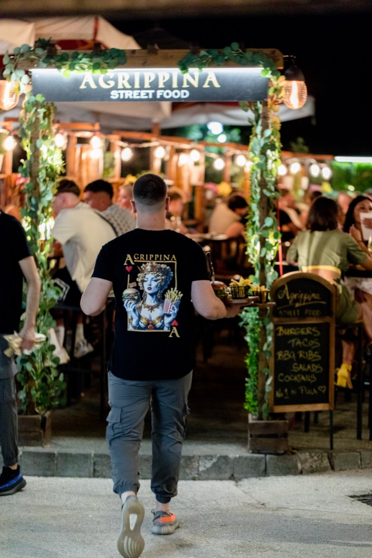 Konobar prolazi ispod osvijetljenog znaka Agrippina Street Food
